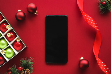 Christmas phone app and holiday message concept. Smartphone with blank black screen and xmas decoration on red background as flat lay mockup design.