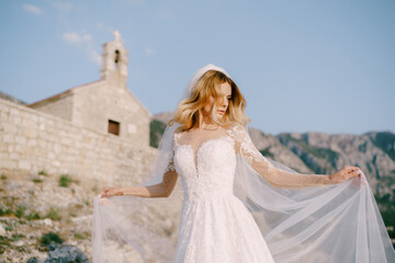 Fototapeta na wymiar Bride in a white lace dress stands against the background of an ancient stone church