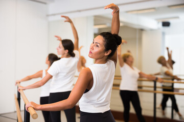 Group of women engaged in classical ballet in a dance studio perfoms a choreographic exercise that...