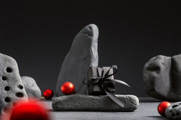 Black gift box on a stone and red Christmas balls. Holiday Xmas background.