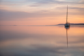 a sailing boat at sunset on a calm lake - obrazy, fototapety, plakaty