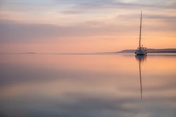 Wandaufkleber a sailing boat at sunset on a calm lake © Matthias
