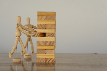 Two wooden puppets rehearsing a wooden block tower and two businessmen strategic plan. Domino...
