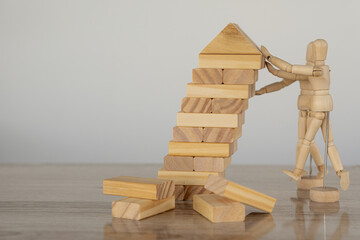 Two wooden puppets are stopping the falling wooden block tower and the strategic plans of two...