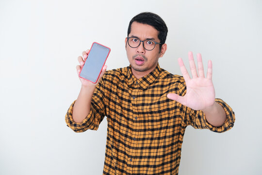 Adult Asian man wearing yellow flannel shirt give stop hand gesture while showing blank mobile phone screen