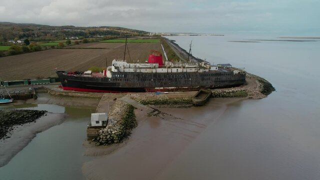 Derelict remains of liner ship docked on sandy coast, aerial orbit view