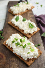 Crispy crackers with cottage cheese and different herbs on wooden board, closeup