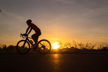 Fototapeta na wymiar a man ride a bicycle at sunset with sunbeam over silhouette trees background