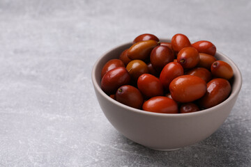 Fresh Ziziphus jujuba fruits in bowl on light table. Space for text
