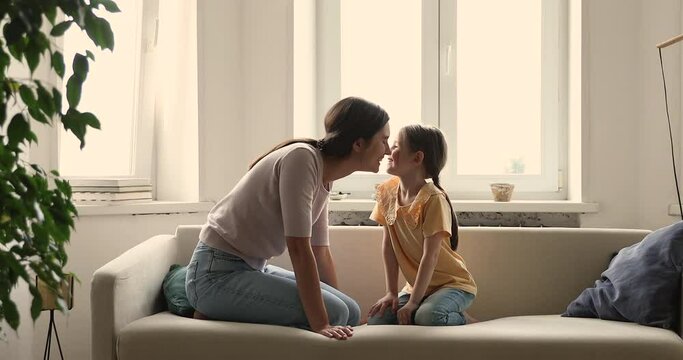 Loving smiling young mother small daughter sit on sofa rub noses express warmth affection having fun. Happy single mom play on couch with adorable girl kidding with child enjoy sweet moment of bonding