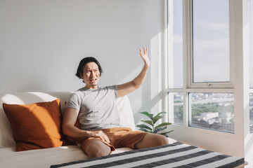 Asian man use his hand to cover the hot sunlight that shine on his living room. 