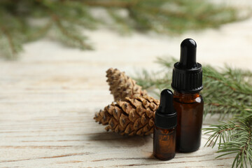 Glass bottles of essential oil, fir branch and cones on white wooden table. Space for text