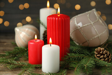Burning candles and festive decor on wooden table against blurred Christmas lights
