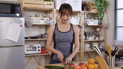 waist up asian young lady in sportswear cutting vegetables with concentration in the morning at home kitchen. staying healthy during self-quarantine. genuine lifestyle