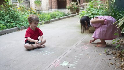 Caucasian boy and asian girl playing, drawing and writing with colored chalk on the floor