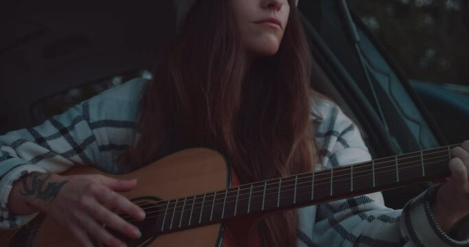Beautiful long haired brunette female gently playing the guitar, close up.