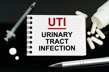 On the black surface are pills, a syringe and a notebook with the inscription - UTI-Urinary Tract Infection