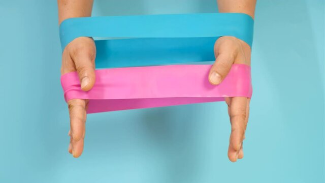 Male hands stretching fitness pink and blue elastic bands.