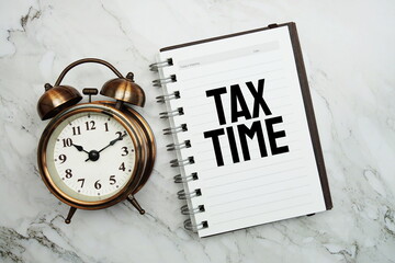Tax Time text on notepad with alarm clock on marble background
