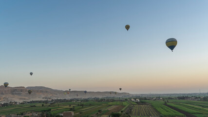 Lots of colorful balloons are flying in the morning sky. Below is the Nile Valley with cultivated fields. A picturesque mountain range in the distance. Egypt. Luxor