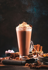 Winter hot chocolate cocoa drink in tall glass with ispices and whipped cream on black table. Dark...