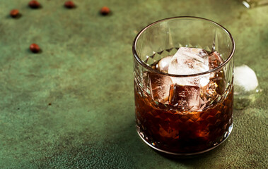 Black russian cocktail, trendy alcoholic drink with vodka, coffee liqueur and ice, rusty green dark background