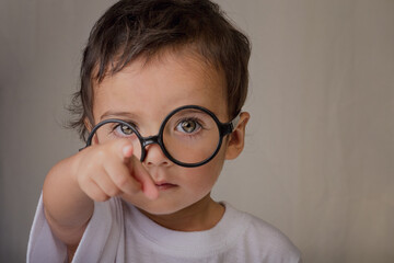 portrait of a smart little boy with big glasses pointing to the front