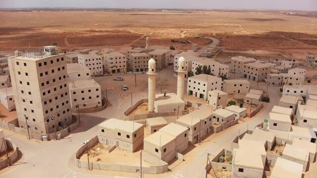 aerial shot of an old empty city in the desert in palestine near Gaza at morning while camera orbit around the buildings and the mosques next to the main squre of the city while a bus driving in it.