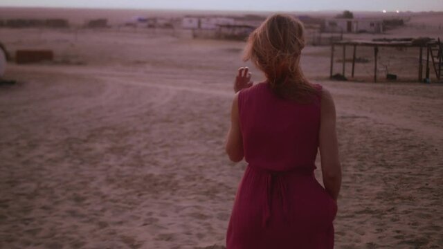 tracking shot of a girl walking in the desert of UAE modeling in front of the camera, wearing nice red dress