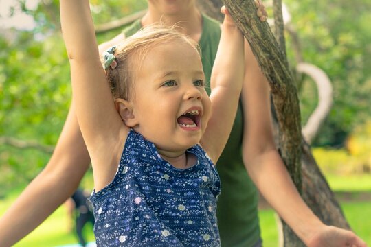 A happy little girl playing at the park and hanging on a tree. - Powered by Adobe