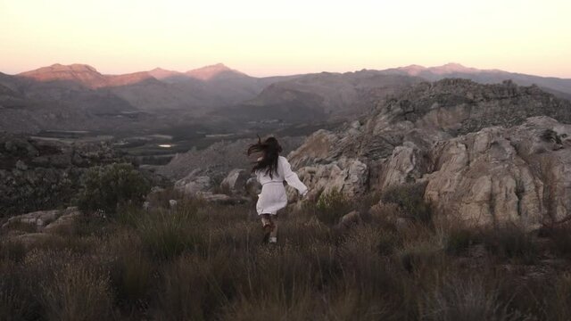Woman running in a rocky semi arid mountain with shrubs around her, freedom and joy concept in the wilderness