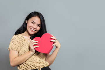 Young woman holding heart shaped gift box with both hands while smiling