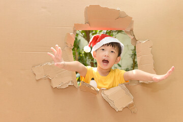 cute little boy wearing santa hat spreading his hands.in the torn paper wall