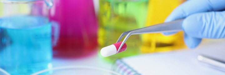 Scientist holds medical pill in forceps in laboratory closeup