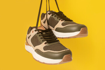 Sports shoes hanging on laces. On a yellow background.
