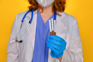 Woman doctor holding cigarette with tobacco in hand, yellow studio background