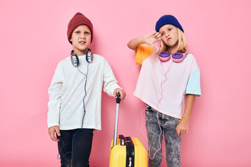 funny little boy and girl yellow suitcase with headphones pink color background