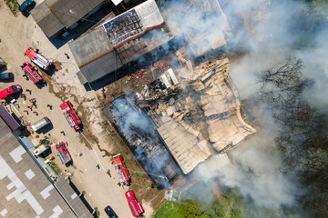 Aerial view of firefighters extinguishing ruined building on fire with collapsed roof and rising...
