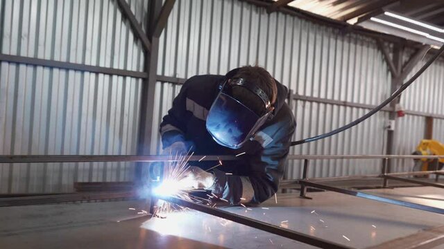 a worker in a protective mask uses a gas welding torch to connect the seam of a metal part at an industrial plant. Blue fire flickers, sparks fly.