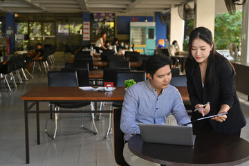 Two businesspeople using laptop computer and discussing about project startup ideas at office.