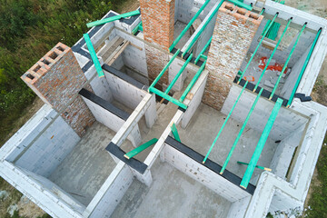 Aerial view of unfinished frame of private house with aerated lightweight concrete walls and wooden roof beams under construction