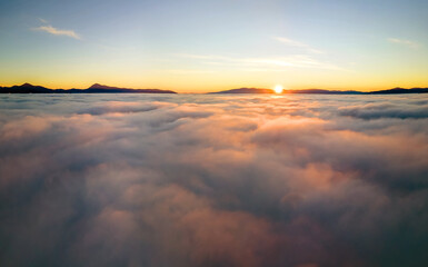 Fototapeta na wymiar Aerial view of vibrant yellow sunrise over white dense clouds and distant mountains on horizon