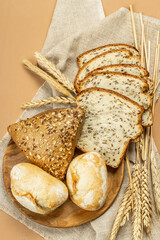 Freshly baked bread with wheat ears, buns, and toasts. Assorted bakery on light beige background