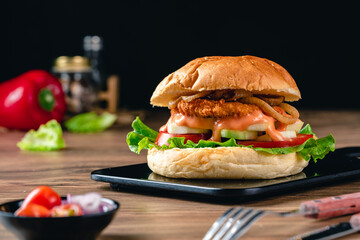 Fresh tasty chicken burger on wood table. Sandwich with chicken burger, tomatoes, pickled cucumber and fried egg. Fresh tasty chicken burger on wooden table.