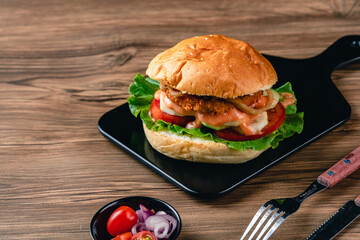 Fresh tasty chicken burger on wood table. Sandwich with chicken burger, tomatoes, pickled cucumber and fried egg. Fresh tasty chicken burger on wooden table.