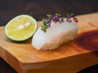 寿司下駄の上のイカの握り寿司。カボスと穂紫蘇を添えたイカの寿司。