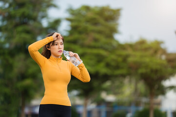 tired woman drinking water after running in park