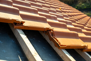 Overlapping rows of yellow ceramic roofing tiles mounted on wooden boards covering residential...