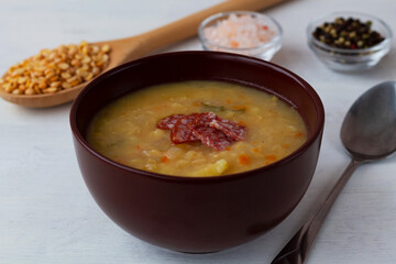 Red lentil soup.The brown bowl of vegetable soup with meat and spices. Pea soup with ham, carrots and potatoes with spoon on a white background. Classic Dutch pea soup erwtensoep, snert with bacon.
