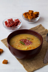 Pea soup with ham and potatoes with spoon on a white background.The brown bowl of vegetable soup with meat and crackers.Classic Dutch pea soup erwtensoep, snert with bacon on the table. vertical.